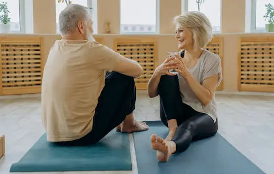 Mature couple sitting on yoga mats smiling and talking in a bright studio with wooden radiator covers