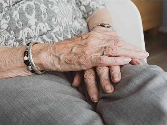Two elderly people holding hands while sitting together, wearing wedding rings and bracelets