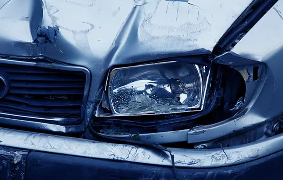 Damaged car front end with broken headlight and crumpled blue hood after collision