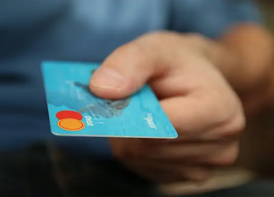 Hand holding blue credit card with red and orange logo circles extending toward camera