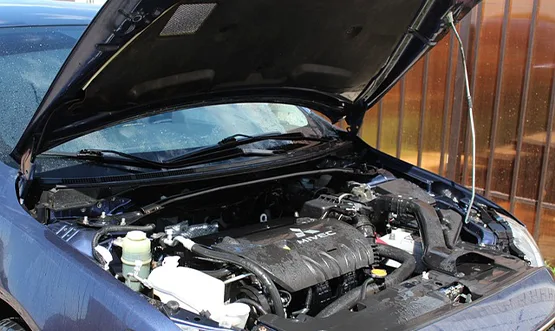 Open car hood revealing engine compartment with modern motor and components against wooden fence background
