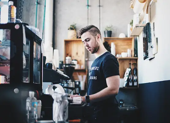 Male barista preparing coffee at espresso machine in modern café