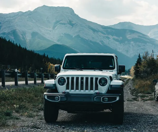White Jeep Wrangler parked on gravel road with mountain range in background