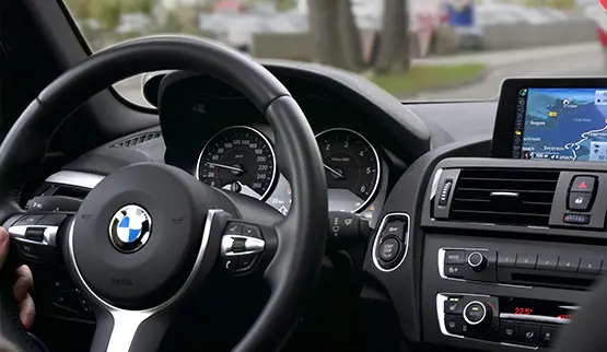 BMW car interior showing steering wheel, dashboard, instrument cluster, and navigation screen from driver's perspective
