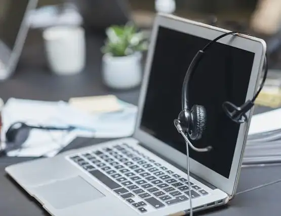 Headset hanging on laptop screen at modern office desk with plant in background