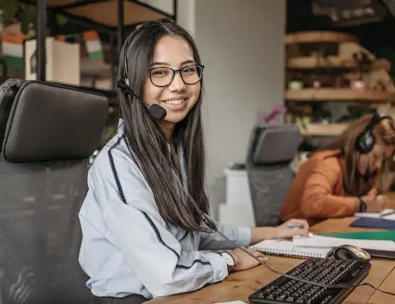 Customer service representative wearing headset and glasses smiling at desk in modern office