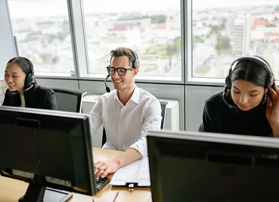 Three customer service representatives wearing headsets working at computers in modern office with city view