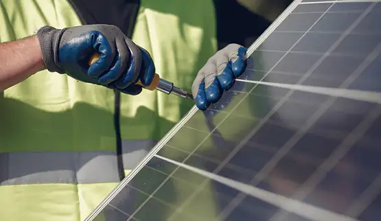 Technician in blue gloves installing solar panel with screwdriver while wearing safety vest