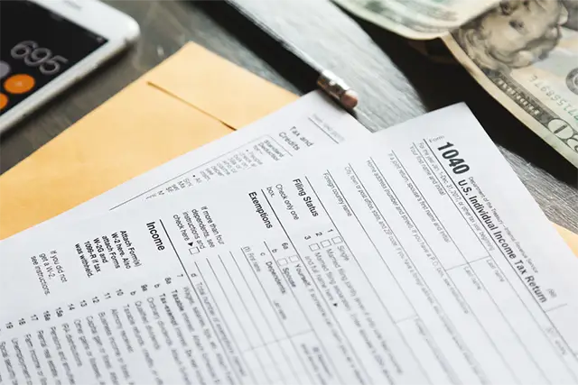 IRS Form 1040 tax document with calculator, pen, and cash on a wooden desk