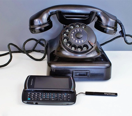 Vintage black rotary dial telephone next to modern Nokia slider phone with QWERTY keyboard