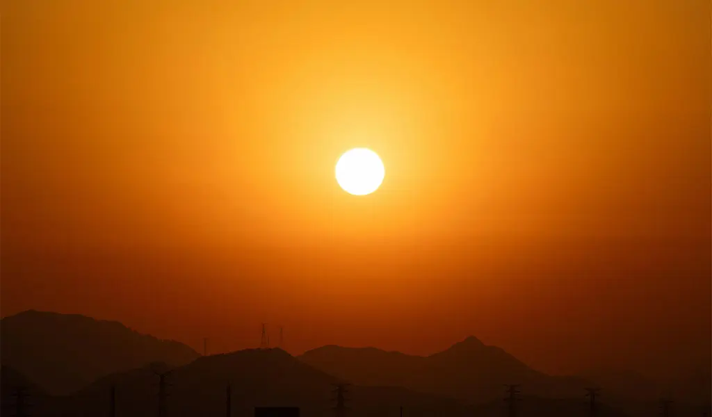 Bright sun setting over silhouetted mountain range with orange and amber gradient sky