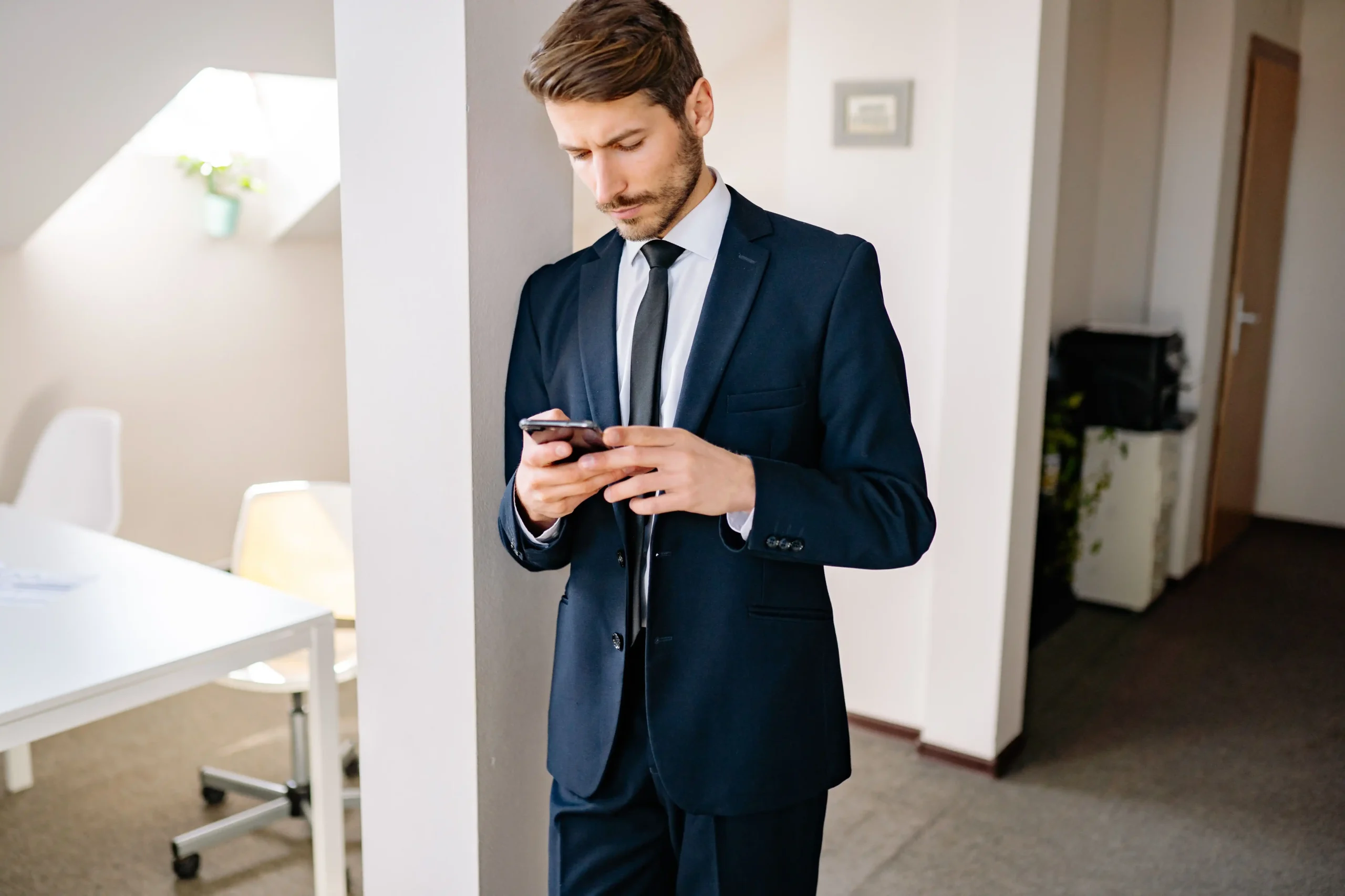 Professional businessman in navy suit checking smartphone in modern office