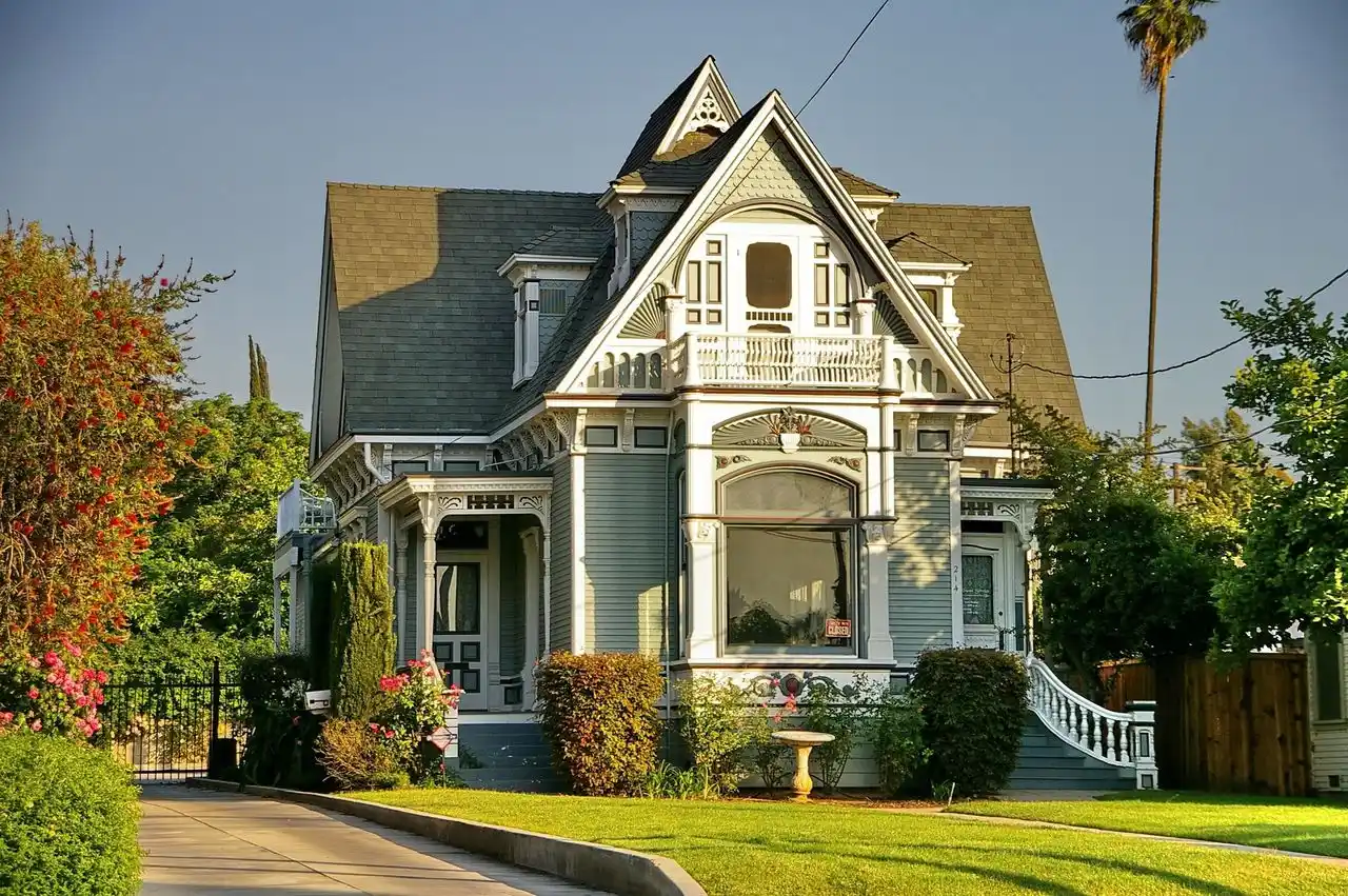 Victorian-style house with ornate white trim, blue-gray siding, steep gabled roof, and decorative balcony