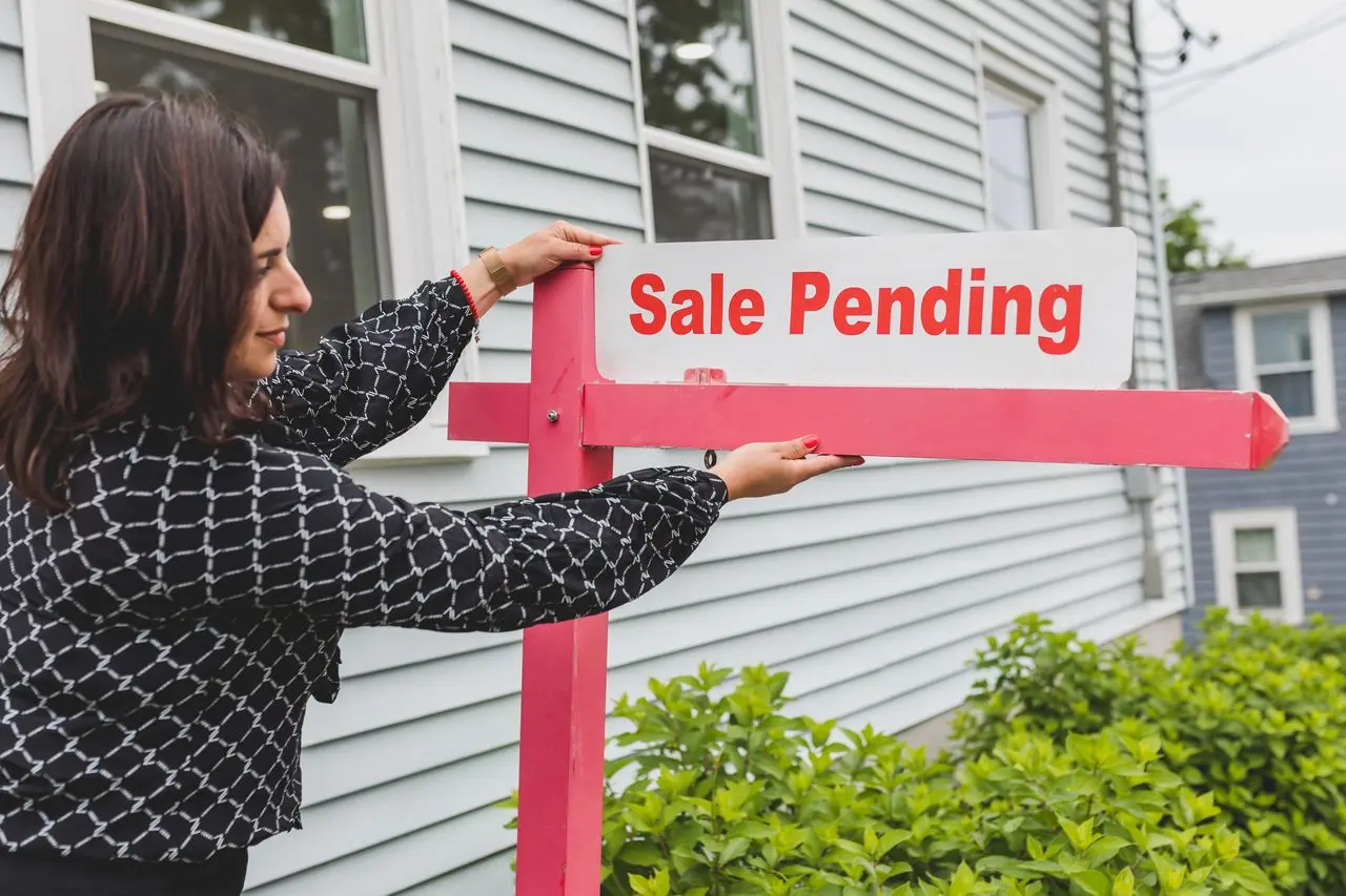Real estate agent placing sale pending sign in front of white house exterior